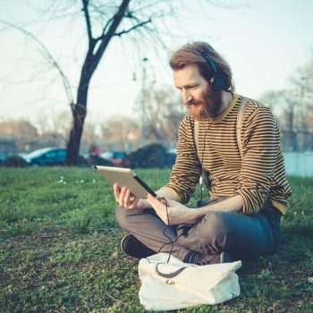 young bearded stylish handsome hipster man using tablet outdoors