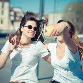 two beautiful young women using smart phone for selfie in the city